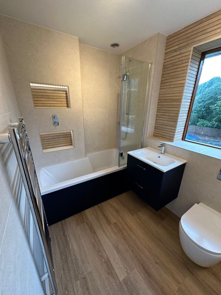 Modern bathroom design features a luxurious bathtub and shower combo, wall niches, floating sink, and toilet. The room boasts wood-style flooring, tiled walls, a large window with striped blinds, and a heated towel rack for ultimate comfort in bathroom installations.